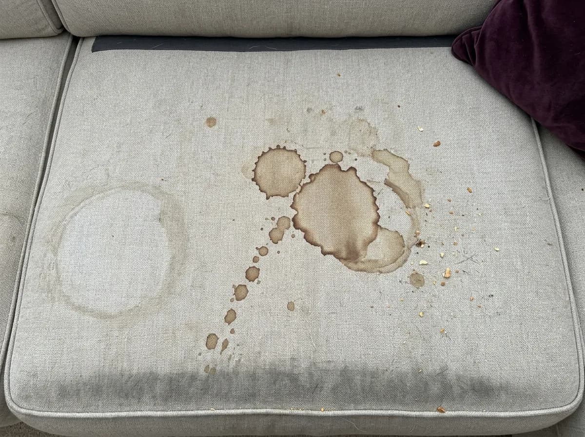 Assento de sofá em tecido cinza-claro com manchas de café e uma película baça